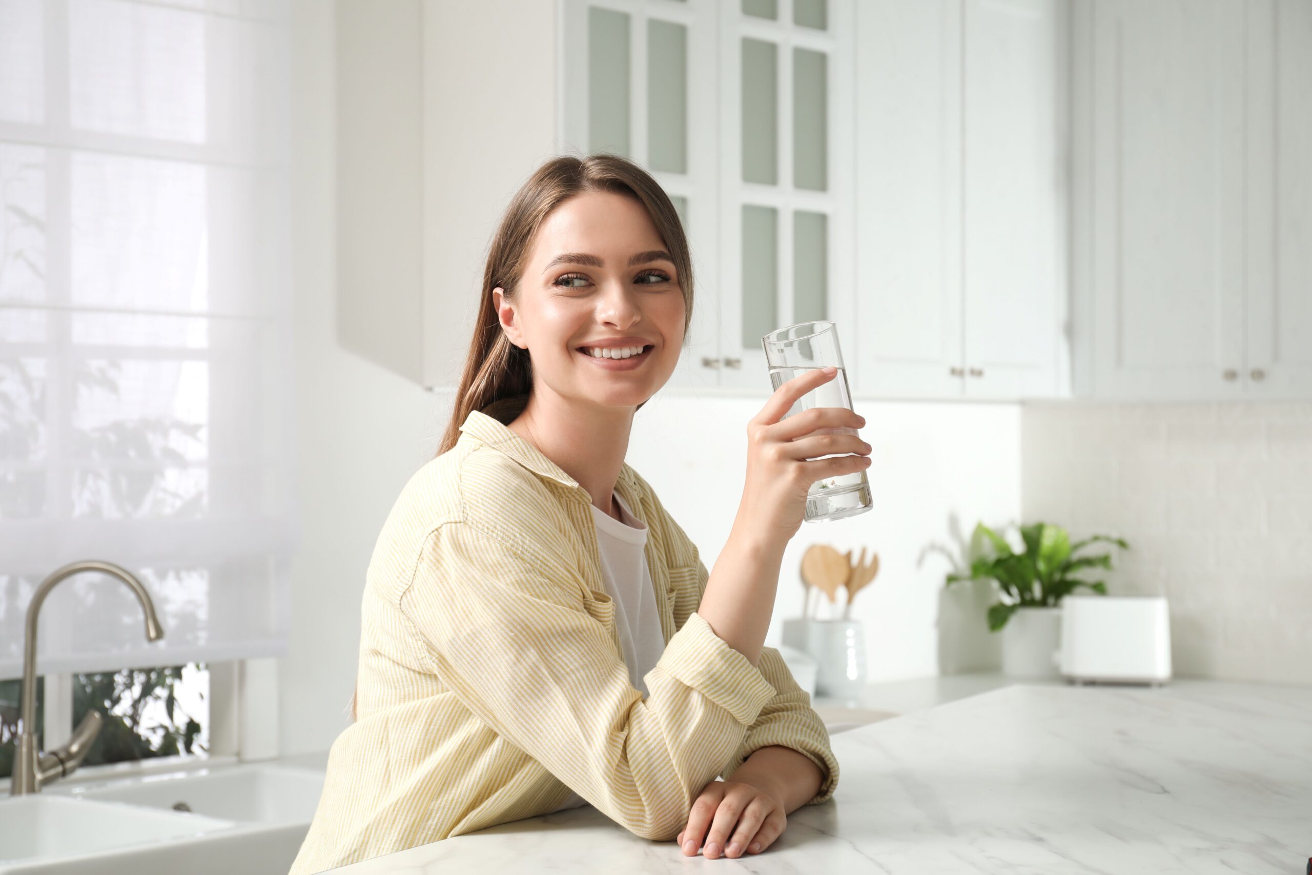 Junge Frau in moderner Küche hält ein Glas sauberes Wasser