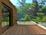 Das Design eines modernen Balkons mit Blick auf einen atemberaubenden tropischen Park. Terrassendielen und Geländer aus gehärtetem Glas. Holzfassade. 3D-Rendering.